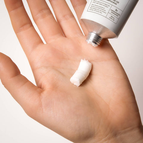 Hand holding a tube of cream of Everist shampoo with a small amount on the palm against a white background