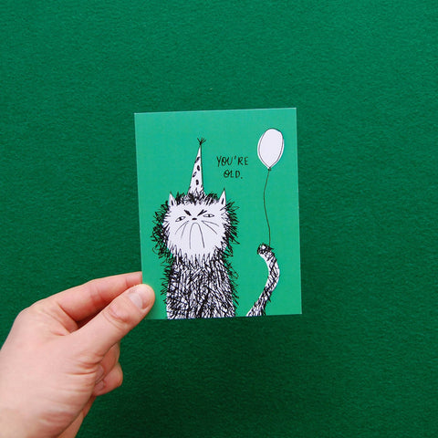 Hand holding a green card with a cat illustration and text against a green background