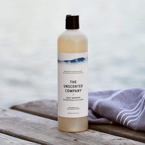 Bottle of 'The Unscented Company' shampoo on a wooden surface with a blurred natural background