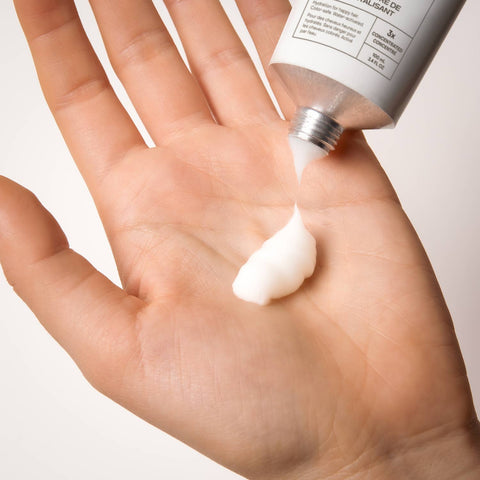 Hand applying Everist conditioner cream from a tube on a light background