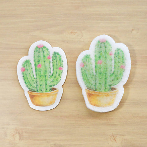Two cactus-shaped stickers on a wooden surface